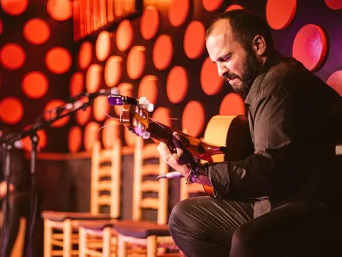 A guitarist playing against a red wall