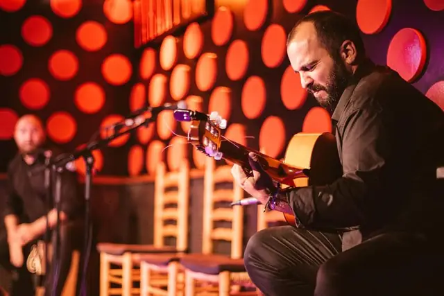 A guitarist playing against a red wall